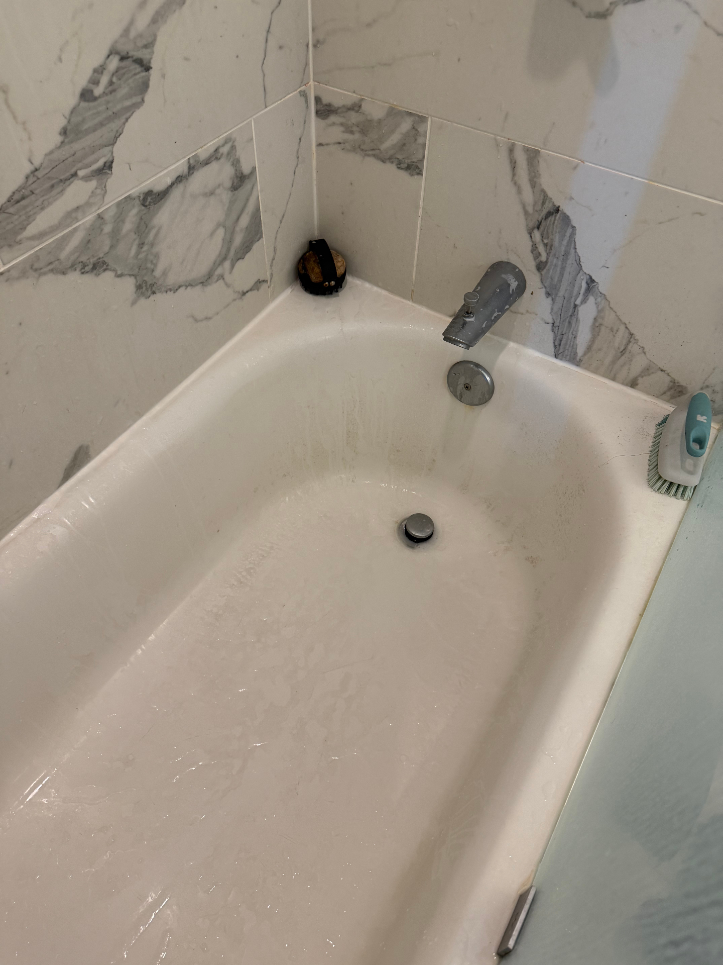 Bathtub with grime buildup and a scrub brush before cleaning