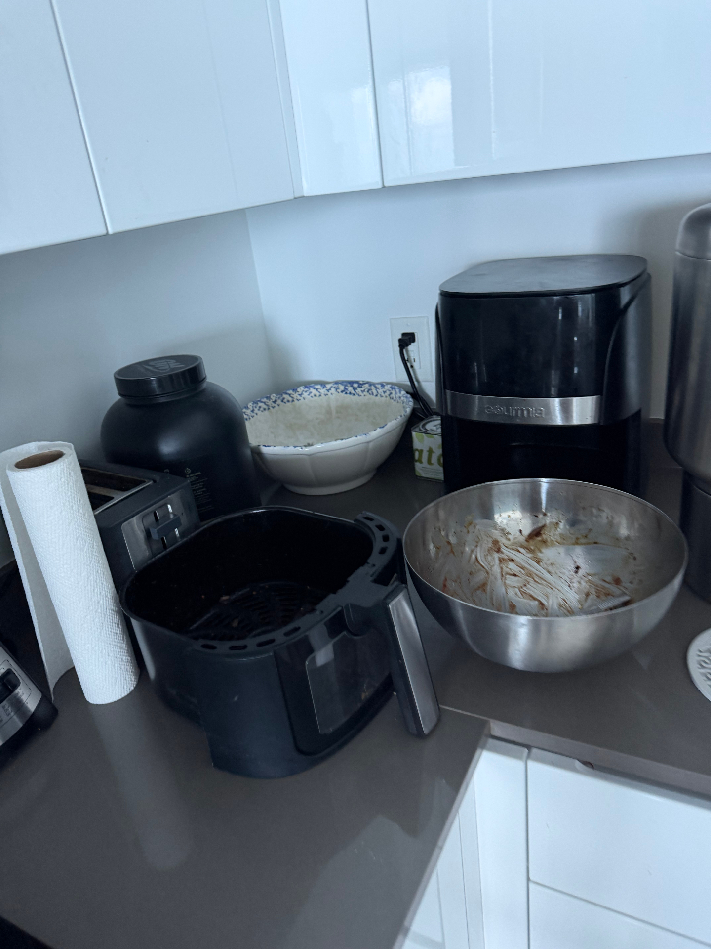Cluttered kitchen counter with a greasy air fryer before cleaning