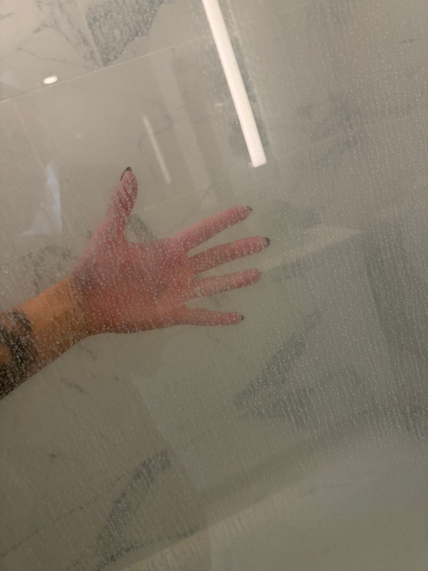 Hand on a foggy, water-spotted shower glass door before cleaning